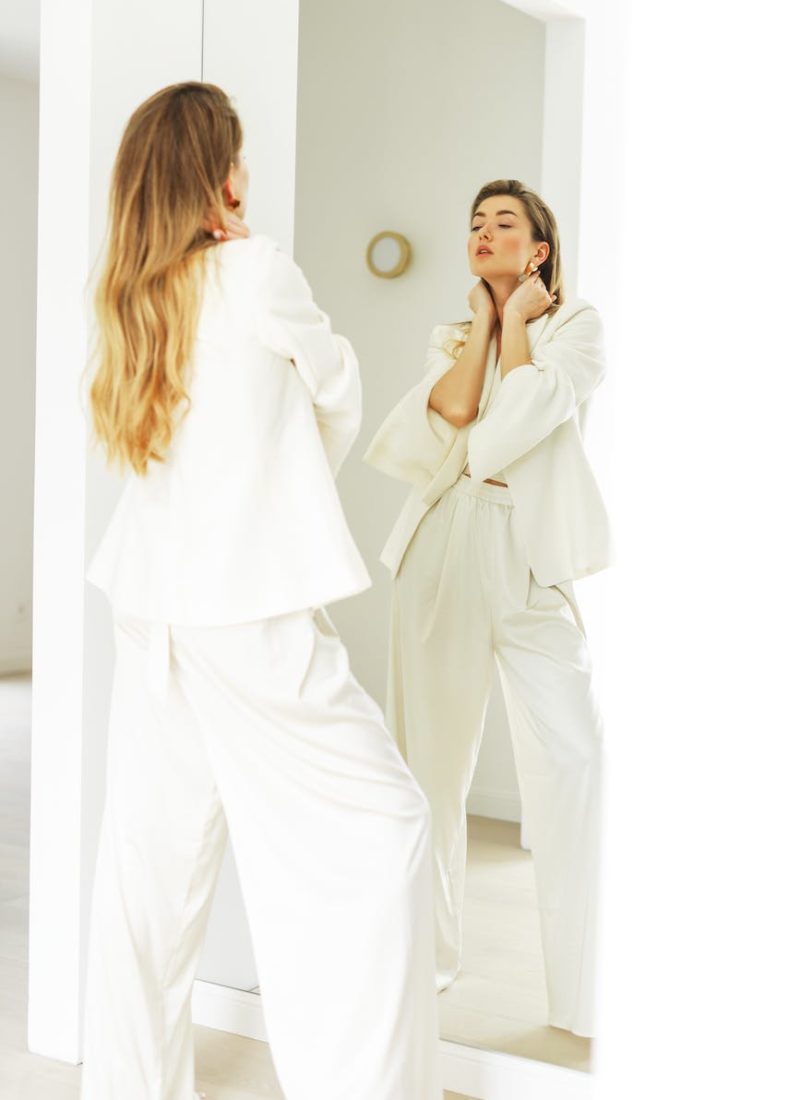 blonde woman in white outfit looking at reflection in mirror