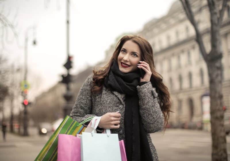 cheerful woman with paper bags making phone call on street