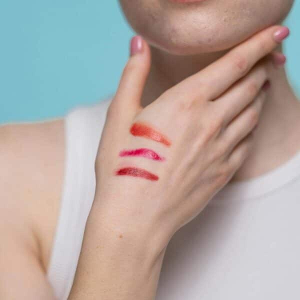 crop photo of woman in white tank top with different shades of red lipstick on hand